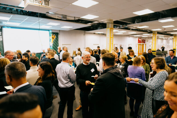 A large group of people at an event. They are swapping coloured cards with one another.